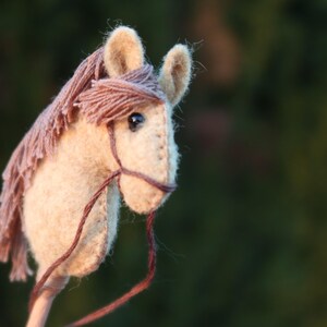 Puede incluir: Un juguete de caballo de balanc&iacute;n de fieltro marr&oacute;n y beige con una brida de cuero marr&oacute;n y un mango de madera.