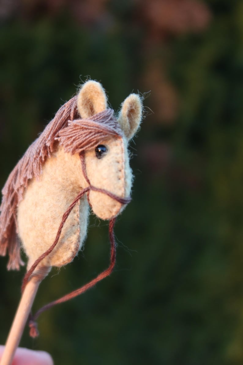 Puede incluir: Un juguete de caballo de balanc&iacute;n de fieltro marr&oacute;n y beige con una brida de cuero marr&oacute;n y un mango de madera.