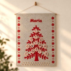 May include: A rectangular light gray felt wall hanging featuring a red felt Christmas tree with small circular photo frames attached to the branches. The name Maria is printed in red above the tree, and red snowflake patterns border the sides.