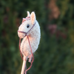 Puede incluir: Un peque&ntilde;o caballo de fieltro beige en un palo. El caballo tiene una brida marr&oacute;n y un ojo negro.
