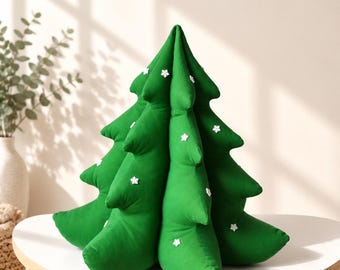 Könnte beinhalten: Ein plüschiges, kegelförmiges Weihnachtsbaumkissen aus leuchtend grünem Stoff. Der Baum besteht aus mehreren geschichteten Zweigen und ist mit kleinen, weißen, sechsstrahligen schneeflockenförmigen Verzierungen auf der Oberfläche versehen.
