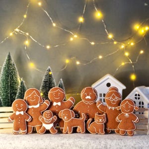 May include: A festive display of gingerbread figures, including a family and pets, arranged in front of miniature Christmas trees and houses. The gingerbread people have white icing details and are set against a backdrop of twinkling lights.