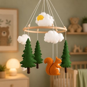 May include: A baby mobile featuring felt clouds, a sun, green trees, and an orange squirrel. The mobile is suspended from a wooden ring with white strings, creating a whimsical forest theme for a nursery.