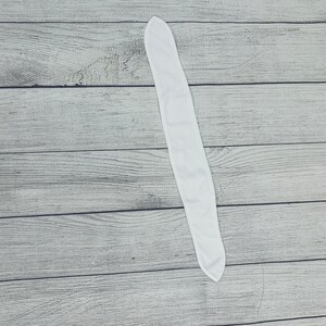 May include: A white fabric headband, folded in half, lying flat on a wooden surface.
