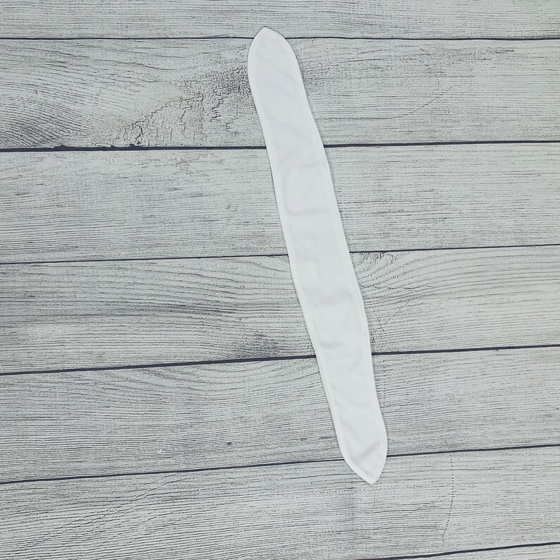 May include: A white fabric headband, folded in half, lying flat on a wooden surface.