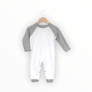 May include: A white baby onesie with grey raglan sleeves. The onesie has a round neckline and snaps at the crotch.