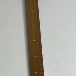 May include: A purple ruler with a sliding clamp and a wooden ruler with markings up to 9 inches.