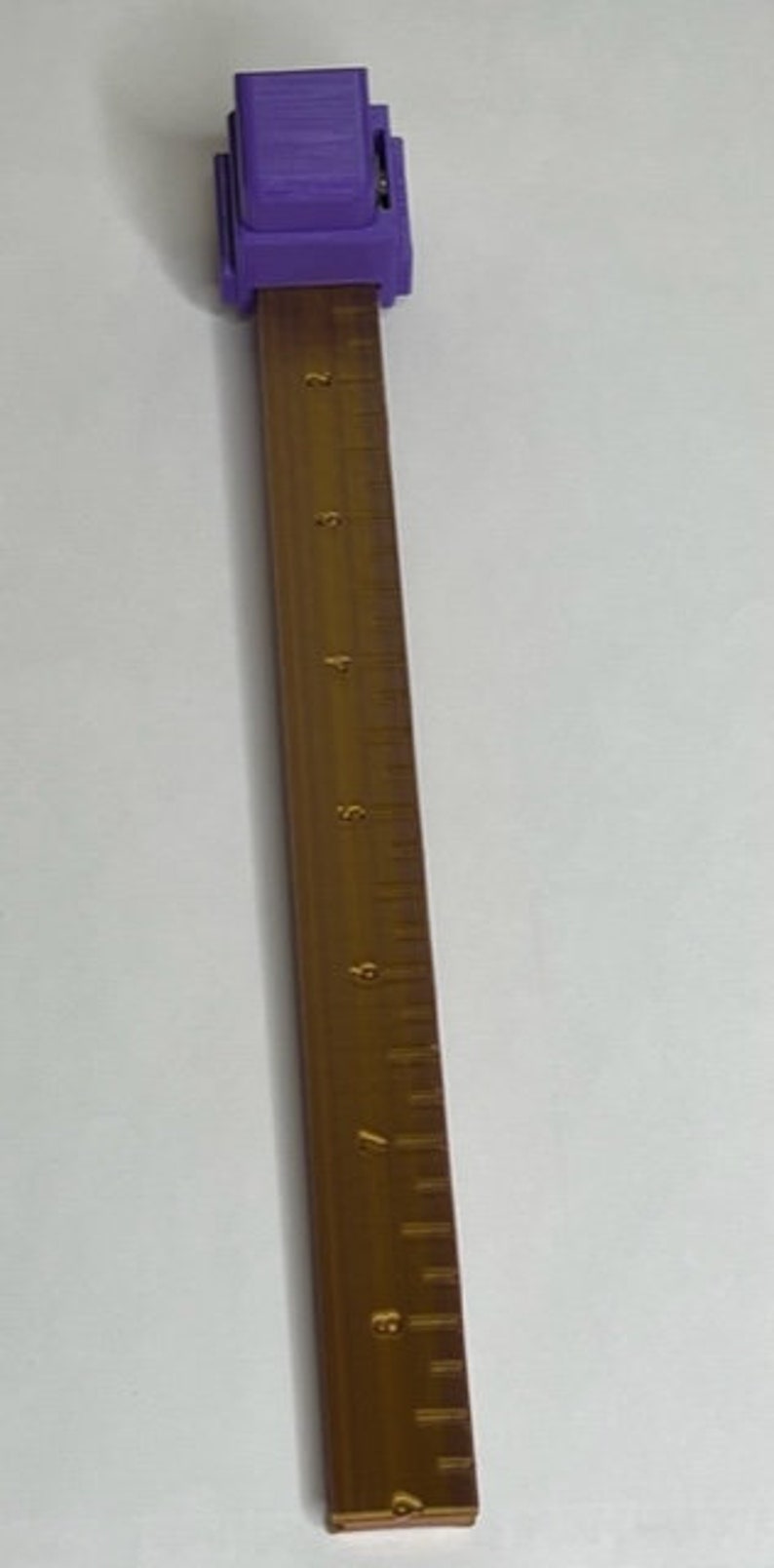 May include: A purple ruler with a sliding clamp and a wooden ruler with markings up to 9 inches.
