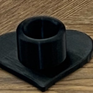 May include: A black heart-shaped candle holder with a round, black candle holder on top.