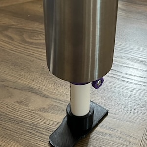 May include: A close-up of a silver metal pole with a black plastic base. The base has a small purple knob on the side. The pole is resting on a wooden floor.