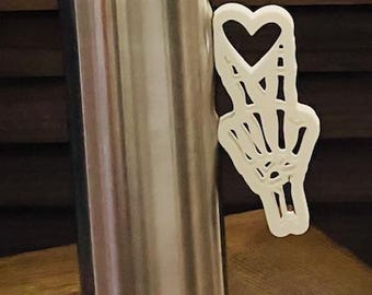 May include: A stainless steel tumbler with a clear lid and a white skeleton hand with a heart design attached to the side.