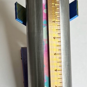 May include: A stainless steel tumbler with a pink, blue, and white patterned design. The tumbler is 9 inches tall and is being measured with a ruler.
