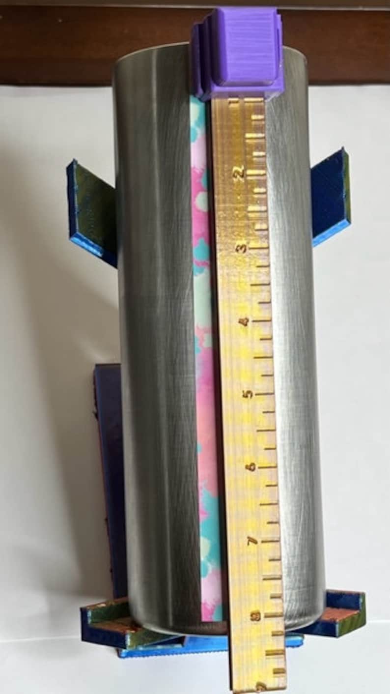May include: A stainless steel tumbler with a pink, blue, and white patterned design. The tumbler is 9 inches tall and is being measured with a ruler.