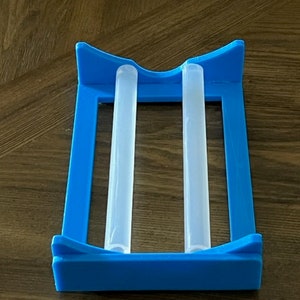 May include: A blue plastic holder with two clear plastic tubes inside. The holder is designed to hold and dry the tubes.