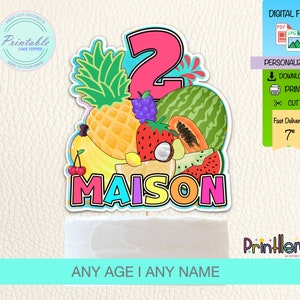 May include: Printable cake topper featuring a colorful number 2 surrounded by tropical fruits, including pineapples, bananas, watermelon, and cherries. The name "MAISON" is written below the number in rainbow colors. The text "ANY AGE I ANY NAME" is at the bottom of the image.