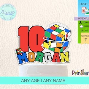 Op de afbeelding: Een taarttopper met het rode getal 10 en de naam "MORGAN" in kleurrijke letters. Het bevat een Rubik's Cube-ontwerp en de tekst "ANY AGE I ANY NAME". De topper is ongeveer 17,78 cm groot.