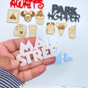 Op de afbeelding: Witte vinyl sticker met de woorden "Main Street" in vetgedrukte blokletters. De sticker wordt in een hand gehouden.