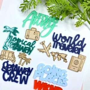 May include: A collection of travel-themed acrylic and wood cutouts. The cutouts feature phrases like "Let's Get Away", "Tropical Getaway", "World Traveler", "Going Places", and "Getaway Crew". There are also cutouts of a suitcase, a palm tree, an airplane, a world map, and a passport.