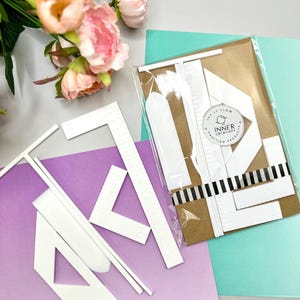 May include: A set of white plastic quilting rulers and templates, including L-shaped and T-shaped tools, some packaged in a clear plastic sleeve on brown cardstock with a circular sticker reading Inner Creativity Let It Flow.