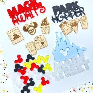 Op de afbeelding: Een verzameling Disney-thema knutselbenodigdheden, waaronder een rood "Magic Always" bord, een zwart "Park Hopper" bord, een blauw "Main Street" bord, een lichtblauw kasteel, een houten kasteelfoto, een houten Mickey Mouse hoofd, een houten koffiebeker, een houten camera, een houten ijshoorn, een houten Mickey Mouse oorboog en een verscheidenheid aan Mickey Mouse oren in rood, geel, zwart en wit.