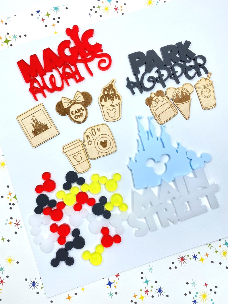 Op de afbeelding: Een verzameling Disney-thema knutselbenodigdheden, waaronder een rood "Magic Always" bord, een zwart "Park Hopper" bord, een blauw "Main Street" bord, een lichtblauw kasteel, een houten kasteelfoto, een houten Mickey Mouse hoofd, een houten koffiebeker, een houten camera, een houten ijshoorn, een houten Mickey Mouse oorboog en een verscheidenheid aan Mickey Mouse oren in rood, geel, zwart en wit.
