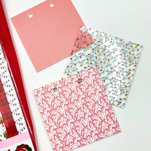 May include: A collection of Christmas-themed gift tags with various patterns. Designs include red and white candy canes, red stripes, and a string of colorful Christmas lights. Each tag has a hole for attaching to a gift.