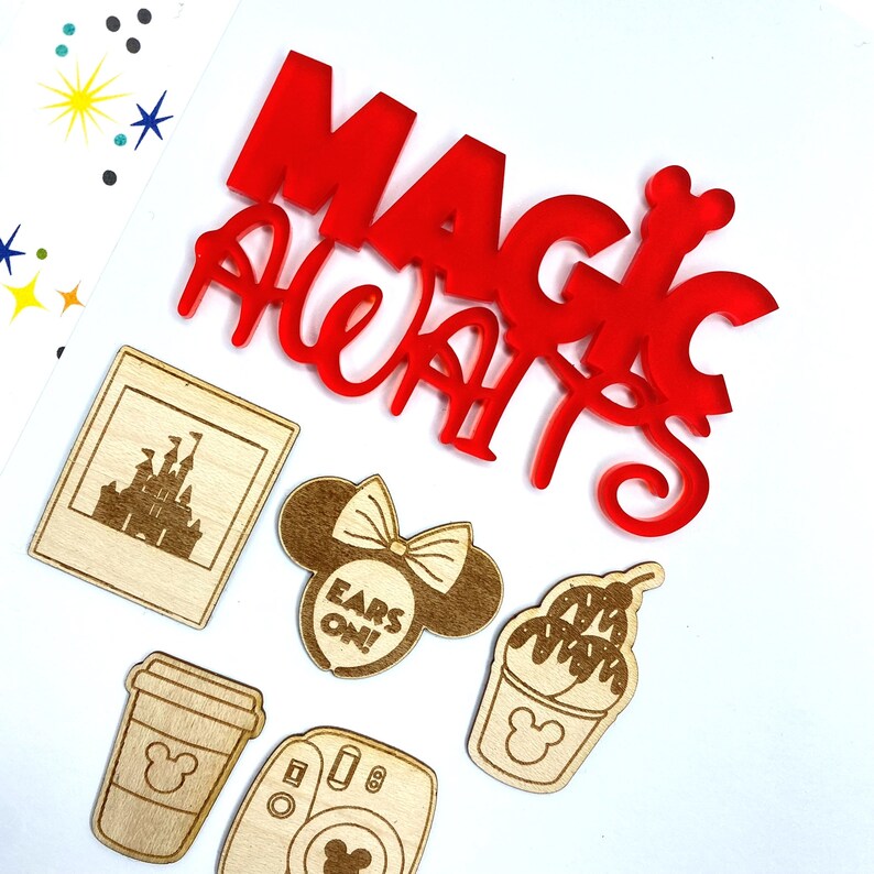 Op de afbeelding: Rood acryl "Magic Awaits" bord met houten uitsnijdingen van een kasteel, Mickey Mouse oren met de tekst "Ears On!", een Mickey Mouse ijshoorn, een Mickey Mouse koffiebeker en een vintage camera.