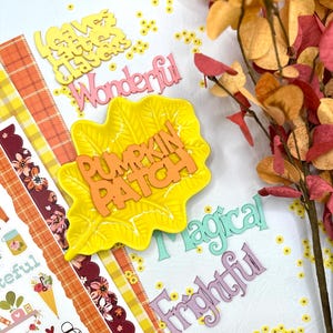 May include: A yellow leaf-shaped ceramic dish with the orange text PUMPKIN PATCH, surrounded by die-cut words including Wonderful, Magical, and Frightful, alongside a strip of patterned paper featuring autumn motifs and a branch with fall-colored leaves.