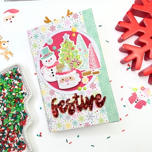 May include: A festive Christmas-themed journal with a colorful snowflake pattern and a red glittery "festive" word. The journal features a snowman, Christmas tree, and Santa Claus mug design. Decorative elements include a red snowflake and Santa Claus stickers.