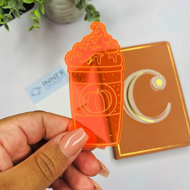 May include: Orange acrylic sticker of a pumpkin spice latte with whipped cream and a pumpkin design on the cup.