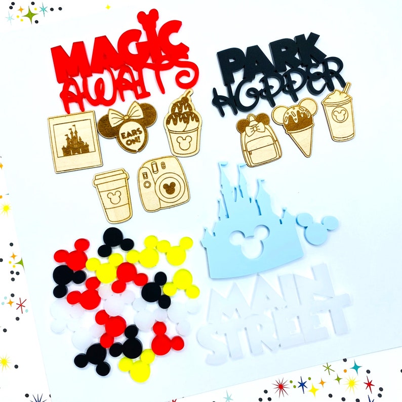 Op de afbeelding: Een set Disney-thema knutselbenodigdheden met verschillende vormen en kleuren. De set bevat een kasteel, Mickey Mouse oren, een koffiebeker, een camera, een Mickey Mouse hoofd en de woorden "Magic Always", "Park Hopper" en "Main Street".