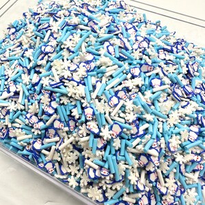 Könnte beinhalten: Nahaufnahme einer Vielzahl von blauen und weißen Polymer Clay Streuseln. Die Streusel umfassen kleine Schneeflockenformen, kleine Pinguinform und lange, dünne blaue und weiße Stäbchen.