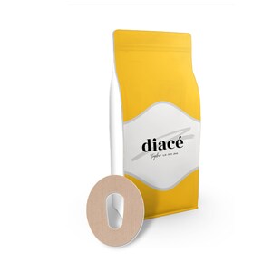 Könnte beinhalten: Ein gelber und weißer Kaffebeutel mit dem Text "diacé" und "Gemeinsam sind wir eins". Im Vordergrund befindet sich ein brauner Papierkreis mit einem Loch in der Mitte.