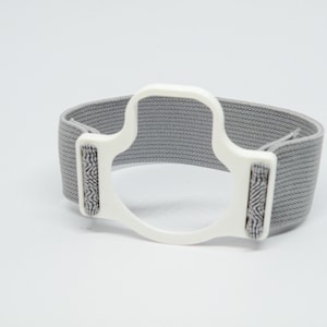 Op de afbeelding: Een witte plastic polsband met een grijs elastisch band. De band heeft een verhoogd, getextureerd ontwerp aan de zijkanten.