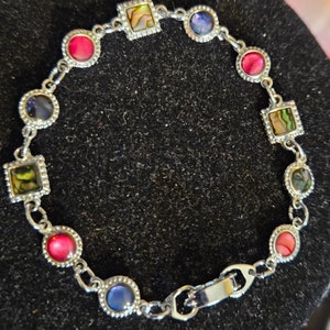 May include: A silver bracelet with a clasp closure. The bracelet features a variety of colorful stones, including red, blue, and green.