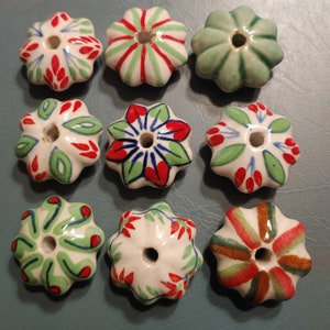 May include: Nine ceramic beads with a flower-like shape. The beads are white, green, red, and blue, with various painted floral designs. One bead is solid green. The beads have a hole through the center.