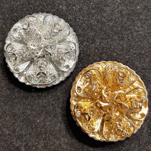 May include: Two decorative metal brooches in the shape of a flower. One brooch is silver and the other is gold.