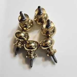 May include: Six shiny, gold-colored cabinet knobs with oval-shaped heads and attached screws. The knobs are arranged in a circular pattern against a white background. These hardware pieces are likely for furniture restoration or new construction.
