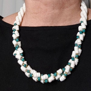 May include: A white and teal blue beaded necklace with a twisted design. The necklace is made of small, round beads and is worn by a person.