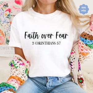 Puede incluir: Camiseta blanca con el texto "Faith over Fear" y la referencia bíblica "2 Corintios 5:7" impresa en negro.