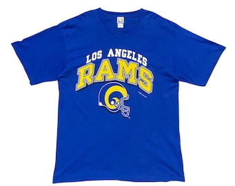 Könnte beinhalten: Ein blaues T-Shirt mit dem Schriftzug "Los Angeles Rams" in weißer und gelber Schrift. Unter dem Text befindet sich ein gelber und weißer Footballhelm.