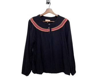May include: Black long-sleeve blouse with a colorful striped neckline and a single button closure. The blouse has a relaxed fit and is made of a soft, lightweight fabric.