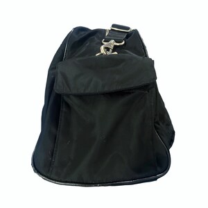 May include: Black nylon travel bag with a zippered pocket and a silver hook closure.