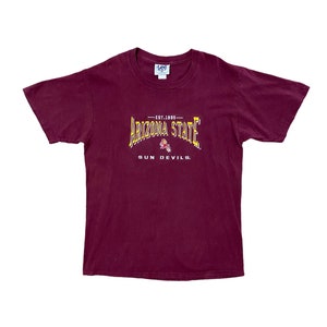 May include: Burgundy short-sleeved t-shirt with a yellow and white graphic of the Arizona State Sun Devils logo. The logo includes the text "EST. 1885" and "SUN DEVILS."