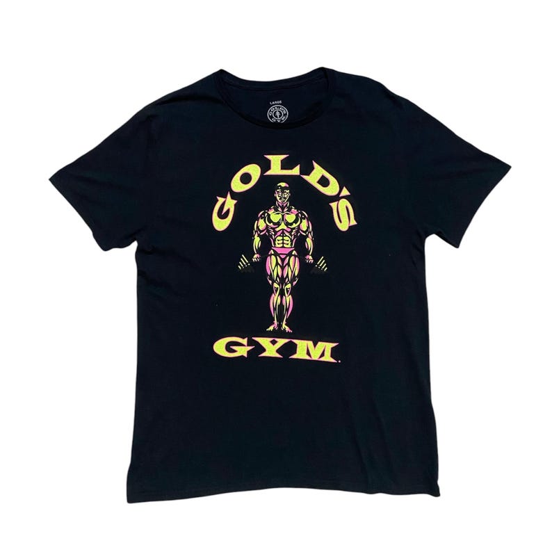 Op de afbeelding: Zwart T-shirt met een gele en roze afbeelding van een bodybuilder die gewichten heft. De afbeelding zegt "Gold's Gym".