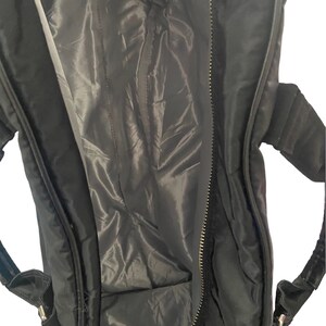 May include: Black zippered travel bag with a black lining and a zippered closure. The bag has two adjustable straps.