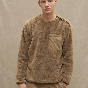 May include: A brown fleece sweatshirt with a zippered pocket on the left side. The sweatshirt has a relaxed fit and a crew neck.