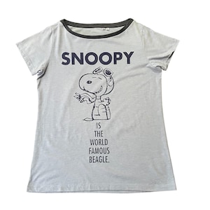 Może przedstawiać: Jasnoszara koszulka z napisem "SNOOPY" nad czarno-białą ilustracją Snoopy'ego w okularach. Poniżej ilustracji znajduje się napis "IS THE WORLD FAMOUS BEAGLE". Koszulka ma ciemnoszary kołnierz i wykończenia rękaw&oacute;w.