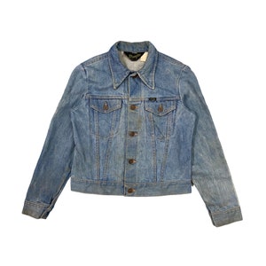 May include: A light blue denim jacket with a button closure and two front pockets. The jacket has a Wrangler label on the collar.