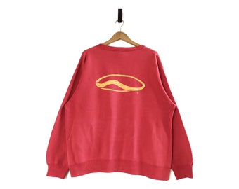 Puede incluir: Sudadera roja con un logotipo amarillo en la espalda. El logotipo es un diseño de onda estilizado.